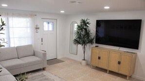 Ein Wohnzimmer mit einer Couch, einem Fernseher, einem Schrank und einer Pflanze.