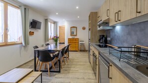 A modern kitchen with wooden cabinets, a stainless steel countertop, and a built-in oven. There is a dining area with a table and chairs, and a TV mounted on the wall. - L'EPICEA - VAL CENIS (VAL CENIS)