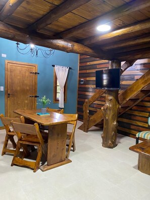 Un coin repas rustique avec une table et des chaises en bois, un escalier en bois et un téléviseur fixé au mur.