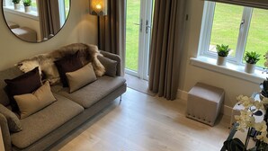 Een gezellige woonkamer met een grijze bank, een ronde spiegel en een raam met gordijnen.