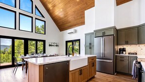 A modern kitchen with a large island, wooden cabinets, and a view of the outdoors. - Epic mountain views, Hot tub and Game room (Bethel)