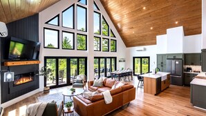 A modern interior with a large living area, kitchen, and dining space with large windows and a fireplace. - Epic mountain views, Hot tub and Game room (Bethel)