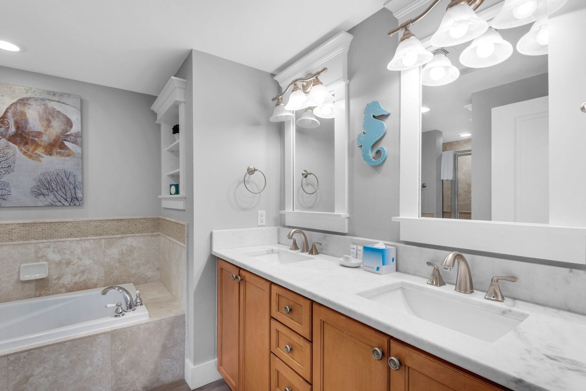 A modern bathroom with a double sink vanity, a bathtub, and a large mirror with lights.