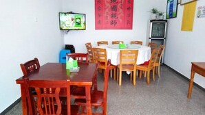 Un comedor con mesas y sillas de madera, un televisor montado en la pared y un estandarte rojo con caracteres chinos.