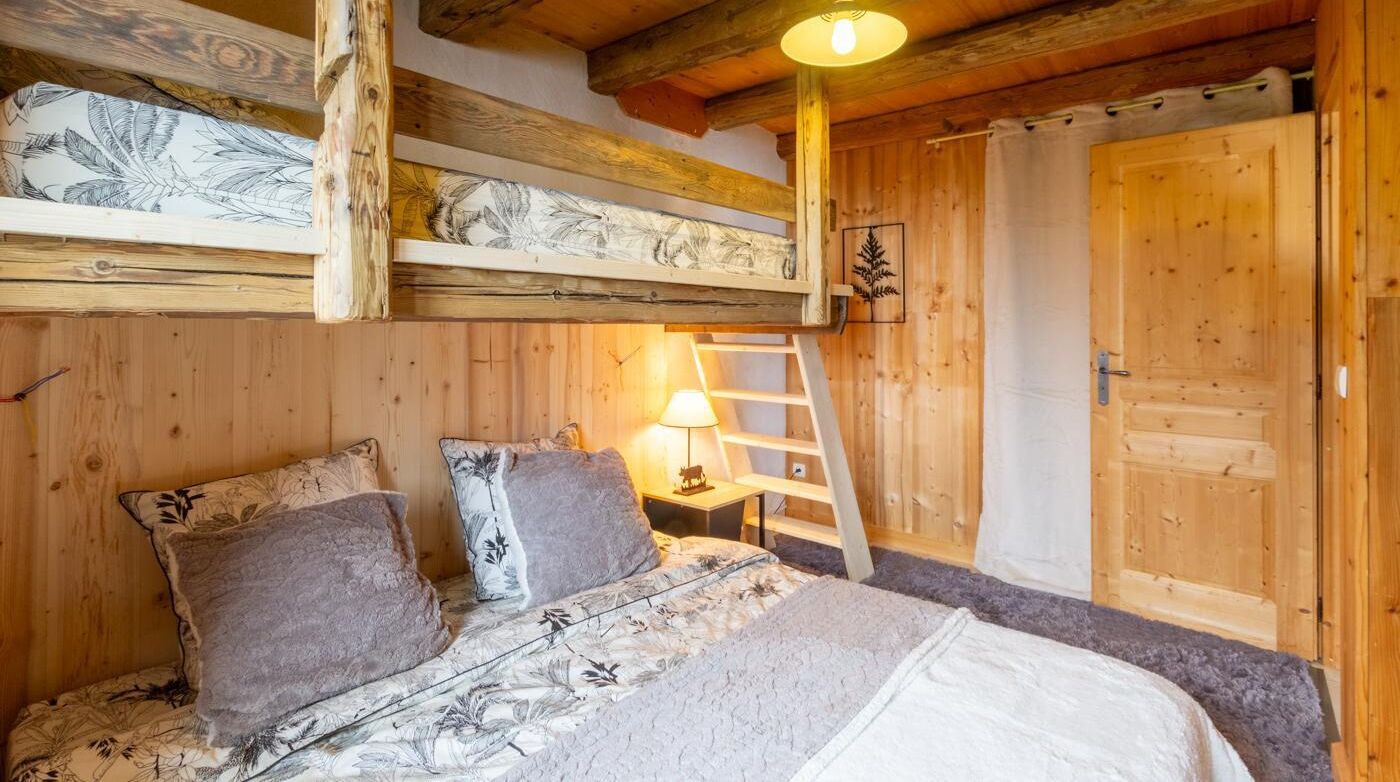 Un dormitorio de cabaña de madera con una litera, una escalera, una lámpara de noche y una puerta.