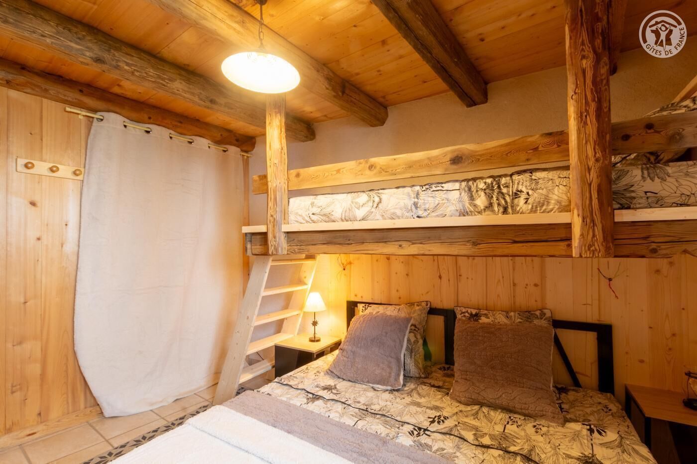 A rustic wooden room with a bunk bed, a small table with a lamp, and a curtain.