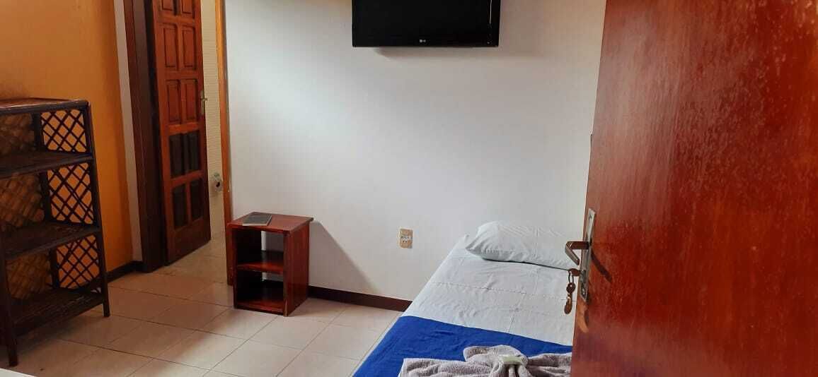 A bedroom with a bed, a TV mounted on the wall, a wooden cabinet, and a small stool.