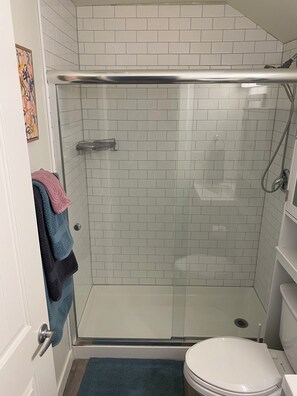 Une petite salle de bain avec une douche à parois de verre, des toilettes blanches et un tapis de bain bleu.