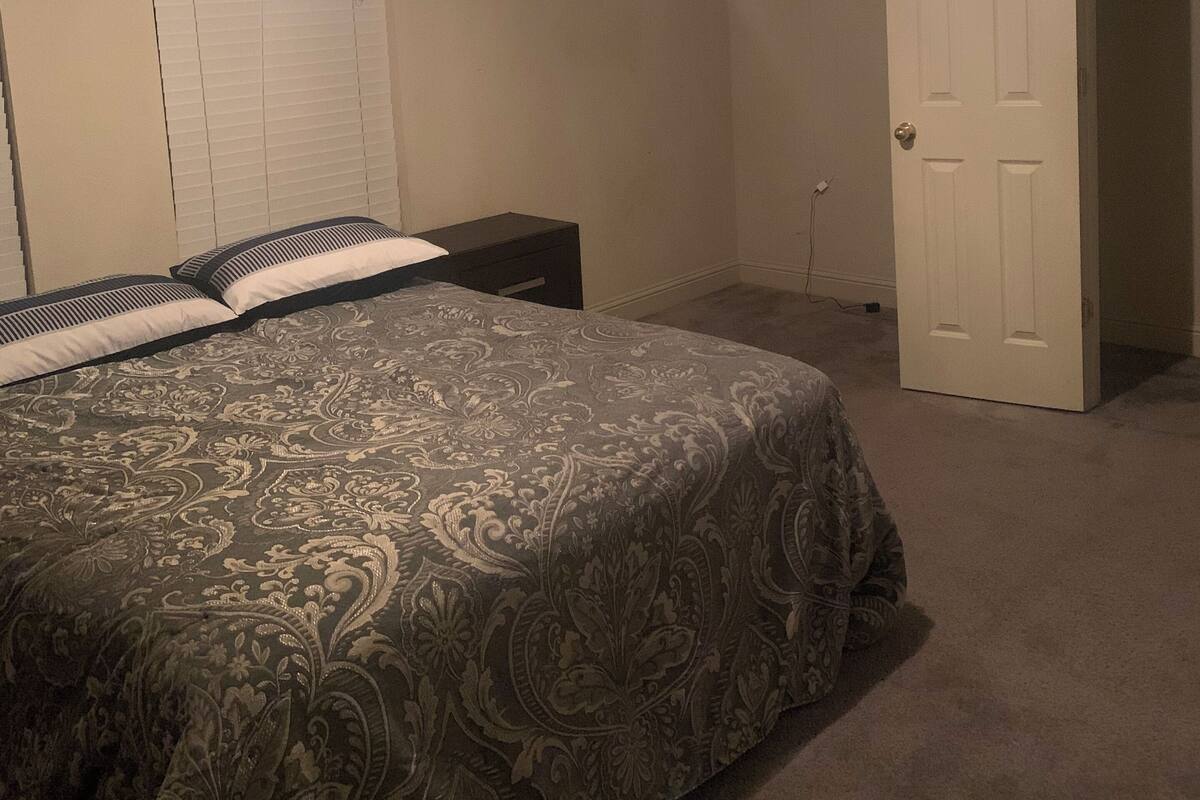 A bedroom with a bed, a nightstand, a closet, and a door leading to another room.