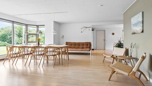 A spacious living area with a dining table, chairs, a sofa, and a large window offering a view of greenery. - Lovely home in Grindsted with lake view (Grindsted)
