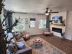 A living room with a sofa, armchairs, a coffee table, a fireplace, a television, and a ceiling fan. - Woodland Pines is a 2-bedroom home located in Mariposa, California. The home features queen beds and accommodates families, couples, and small groups. (Mariposa)