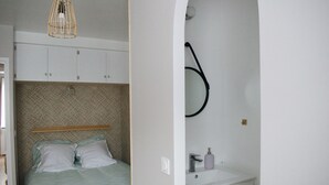 A bedroom with a bed, a hanging light fixture, and a bathroom with a sink and mirror.