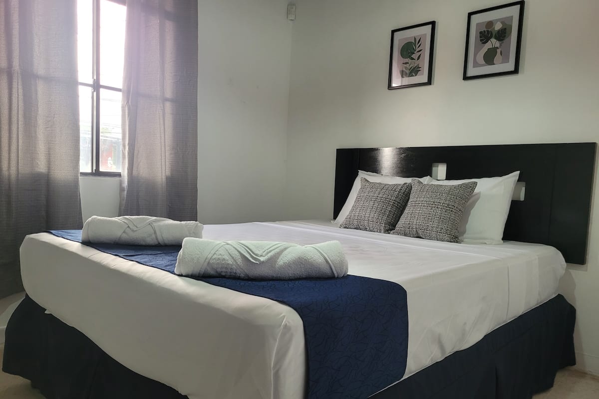 A neatly made bed with white and blue bedding, two pillows, and a blue throw blanket.