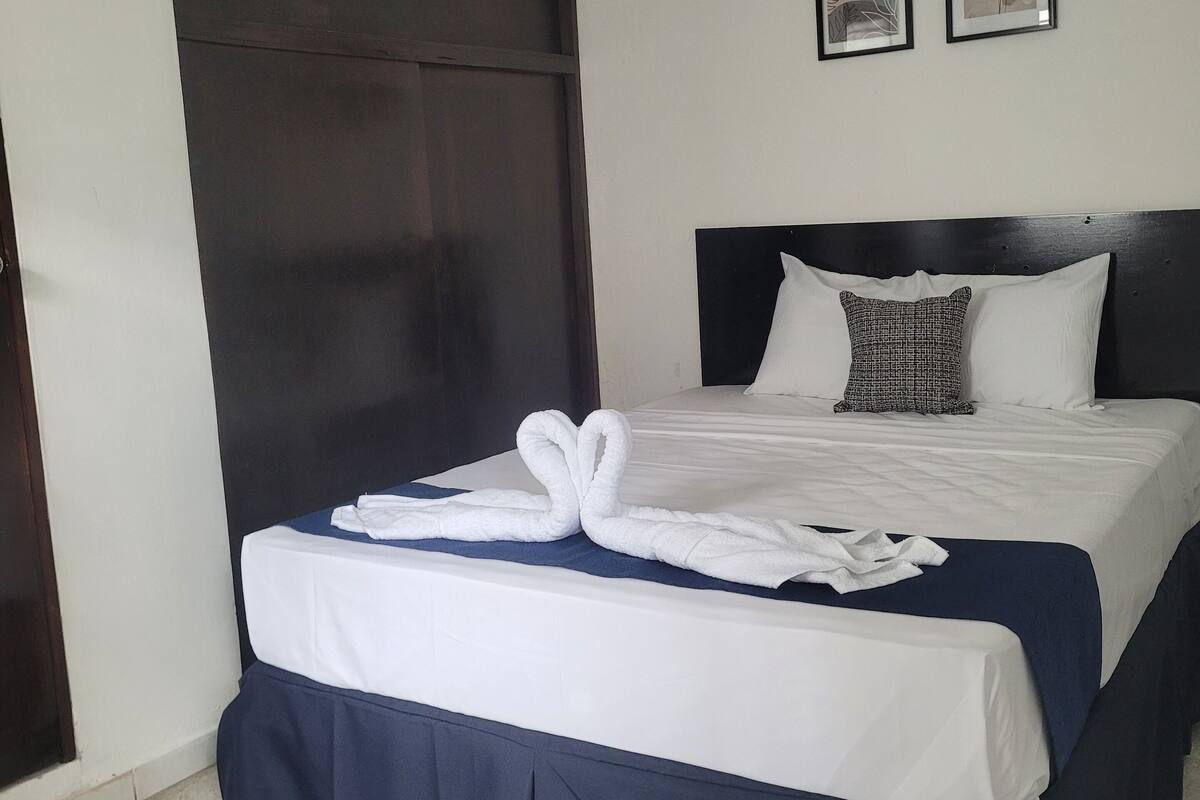 A hotel room with a large bed, dark headboard, white bedding, and two framed pictures on the wall.