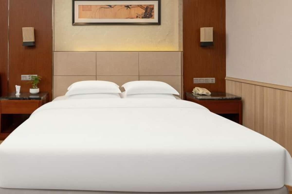 Habitación de hotel con cama, dos mesitas de noche, teléfono en la pared y una obra de arte enmarcada sobre la cama.