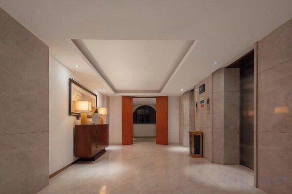 Un vestíbulo de hotel con una recepción, un cuadro enmarcado y una puerta que da a un ascensor.