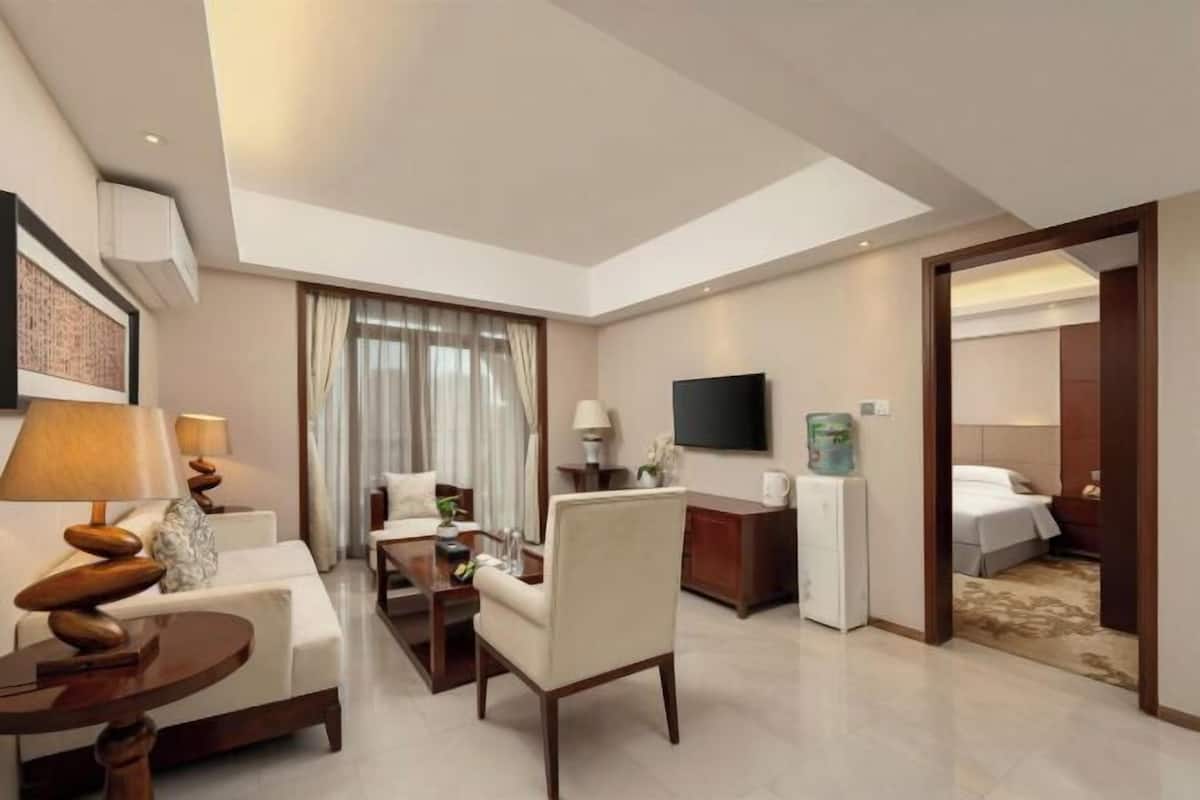 Una habitación de hotel con sofá, sillón, mesa de comedor, televisor y cama.