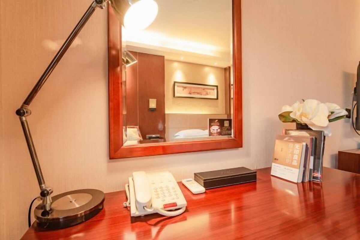 Ein Hotelzimmer mit einem Holztisch, einem Telefon, einer Fernbedienung, einem Spiegel und einem gerahmten Bild an der Wand.