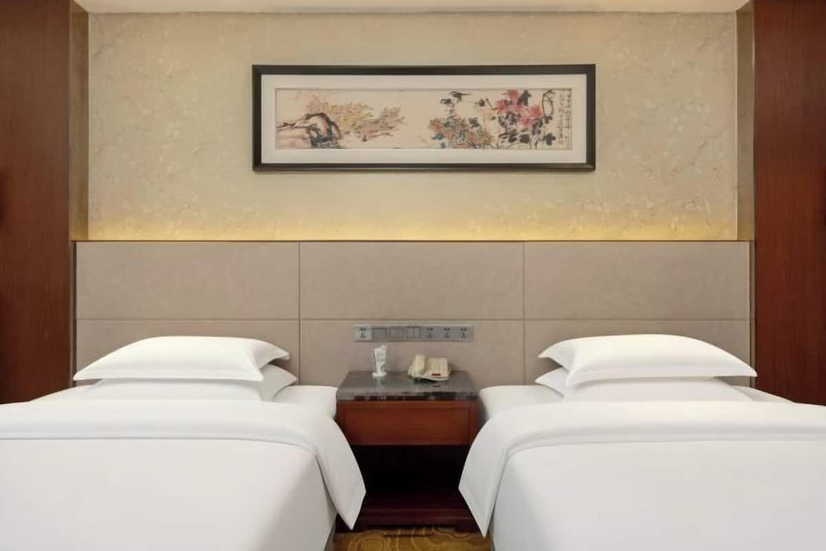Habitación de hotel con dos camas, una mesita de noche, una obra de arte enmarcada en la pared y un panel de control sobre la mesa.
