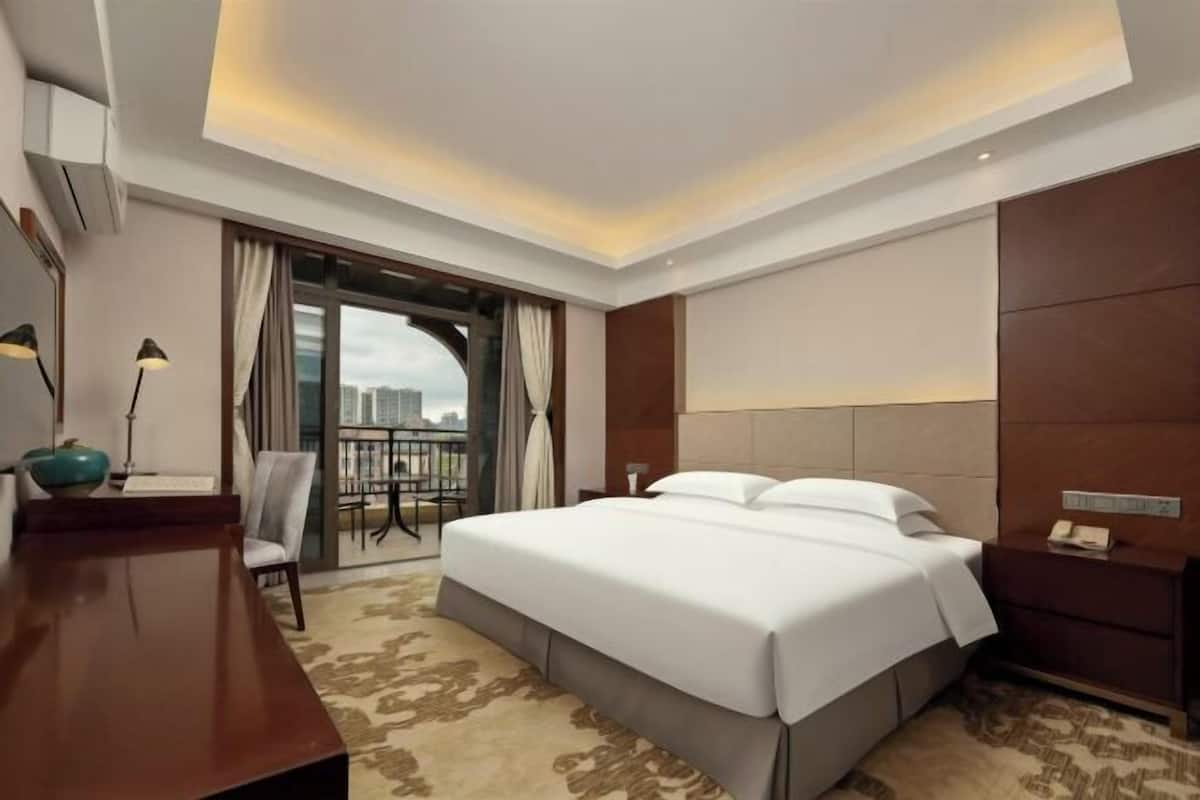 Habitación de hotel con una cama grande, un escritorio, una silla, un balcón con vistas y un diseño de techo moderno.