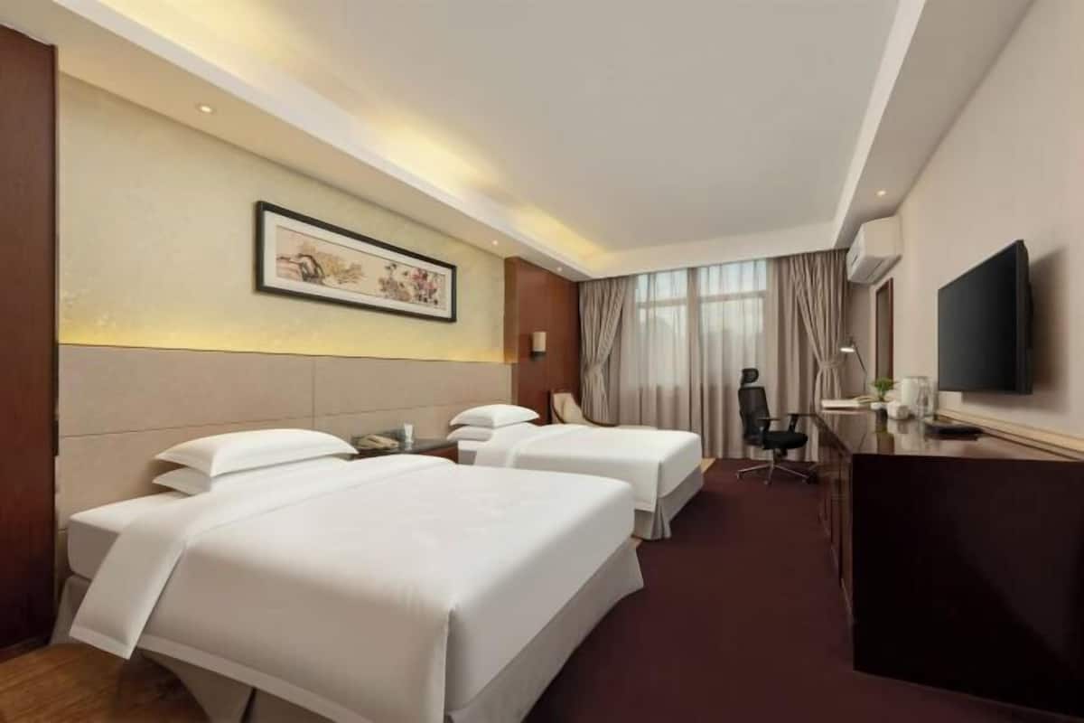 Habitación de hotel con dos camas, un escritorio, una silla, un televisor y un cuadro en la pared.