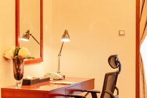 Ein Hotelzimmer mit einem Holztisch, zwei Schreibtischlampen, einem Telefon, einer Vase mit Blumen und einem Stuhl.
