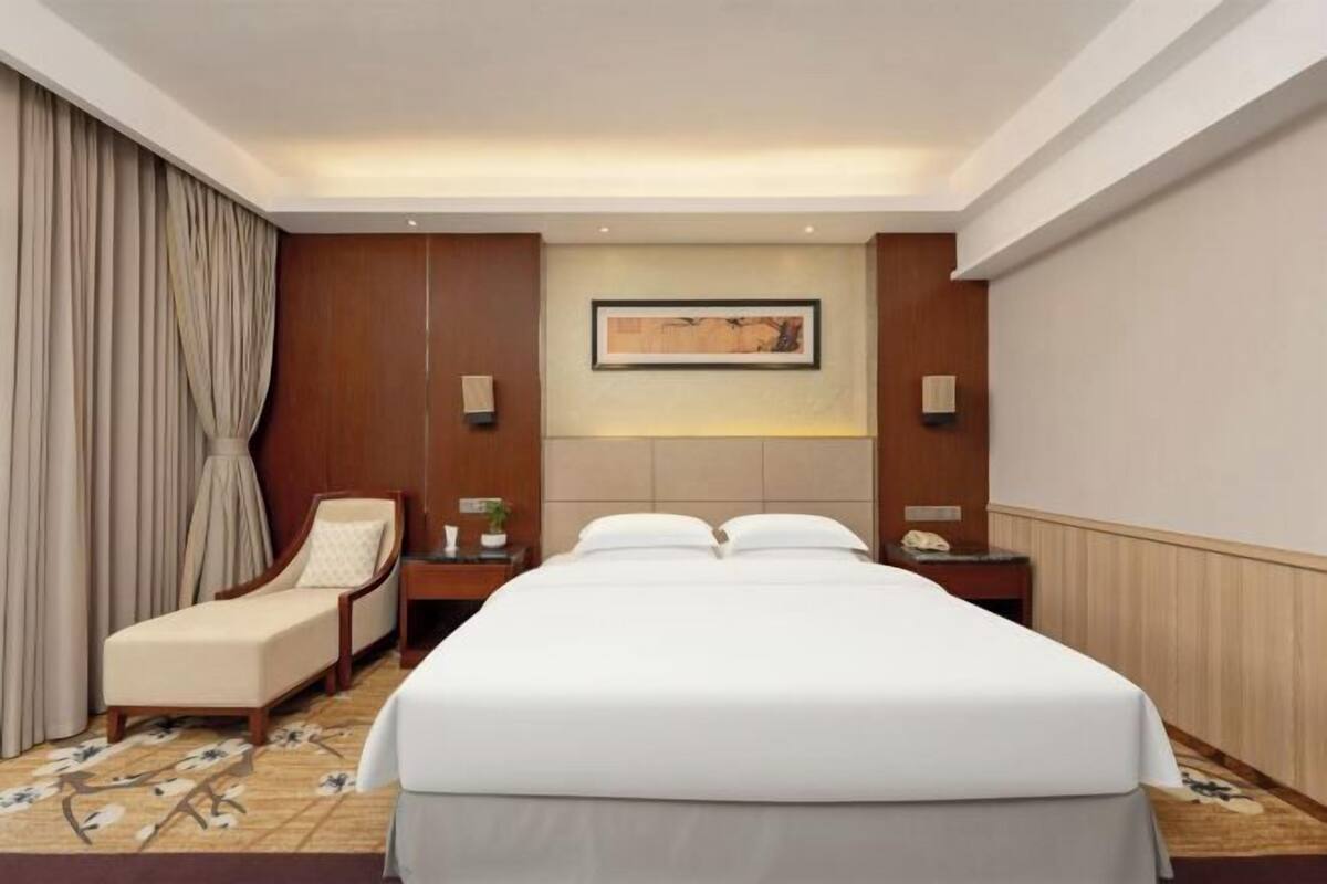 Una habitación de hotel con una cama grande, una silla, una mesita de noche y un cuadro colgado en la pared.