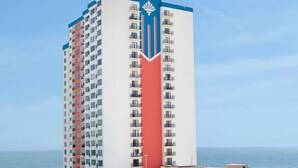 A tall hotel with a distinctive logo on the side, multiple balconies, and a view of the sea.