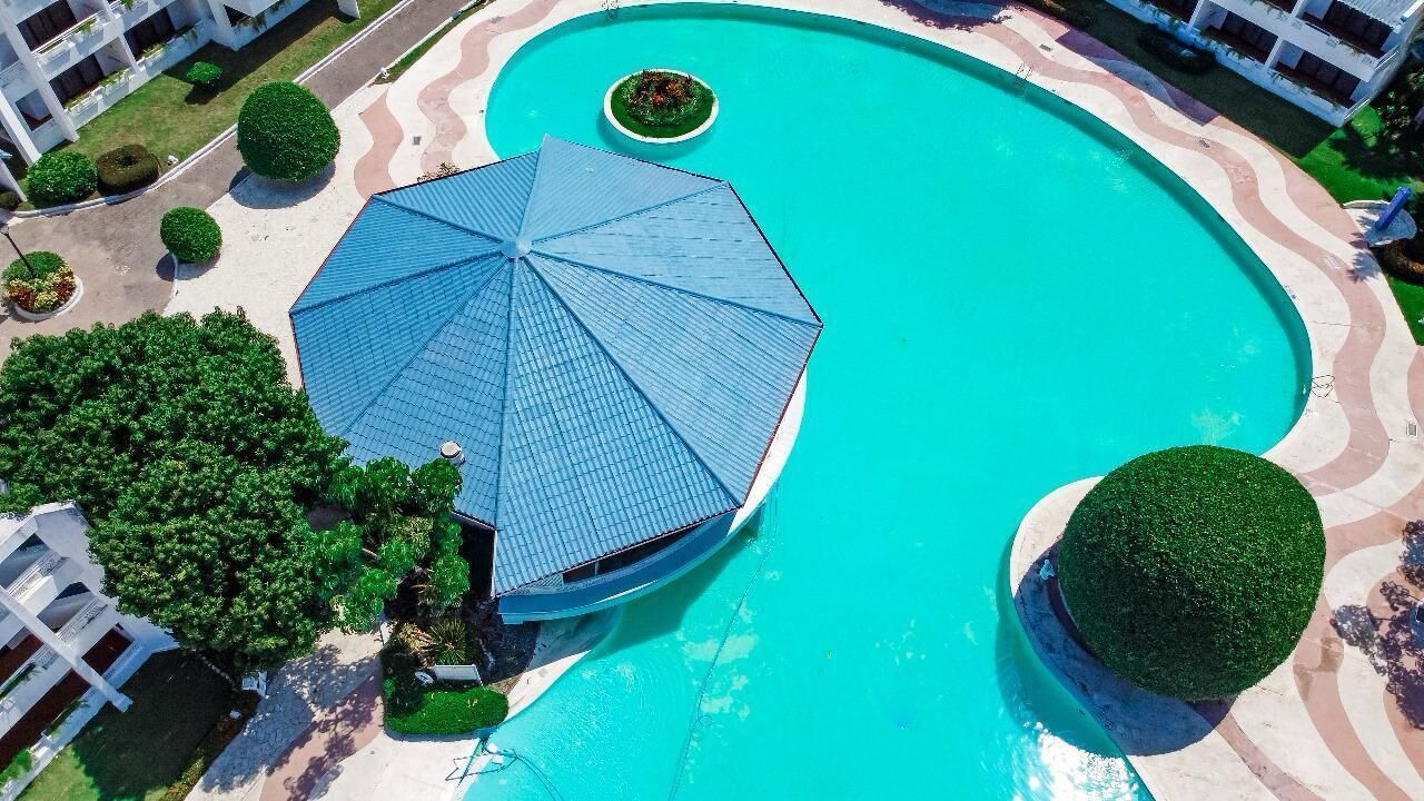 An aerial view of a swimming pool area with a large blue umbrella, surrounded by well-maintained greenery and modern buildings.