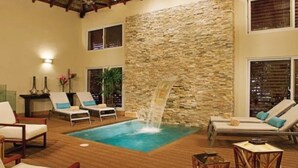 A pool area with lounge chairs, a waterfall feature, and a stone wall. - Riviera del Mar (Puerto Plata)