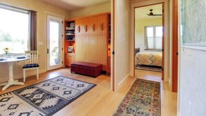 A room with a wooden wardrobe, a red bench, a patterned rug, a small table with a chair, and a bed with a patterned bedspread. - Stunning mountain views, quiet, peaceful, unique, private attached guest suite (Bend)