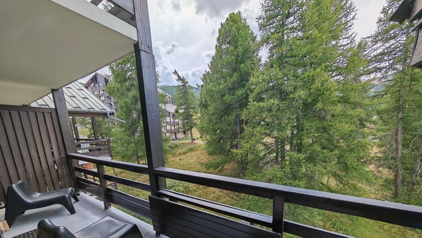 A balcony with a view of a forest and residential buildings. - Spacious, modern 4-room duplex apartment, comfortable, quiet, ski in, ski out (Risoul 1850)