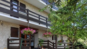 A two-story building with a stone facade, a wooden balcony, and a gravel driveway. - Spacious, modern 4-room duplex apartment, comfortable, quiet, ski in, ski out (Risoul 1850)