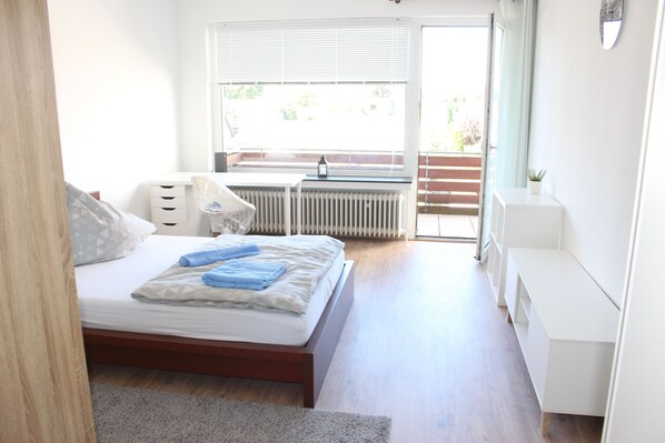 A bedroom with a bed, a radiator, a window, and a door leading to a balcony.