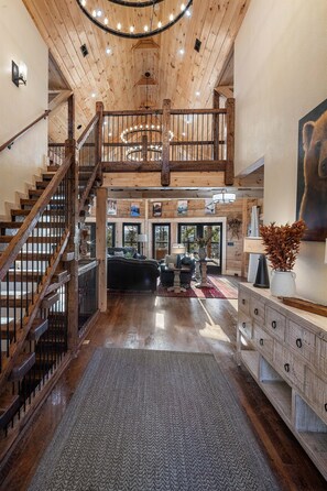 Un interior espacioso con una escalera de madera, una sala de estar con chimenea y vistas al exterior.