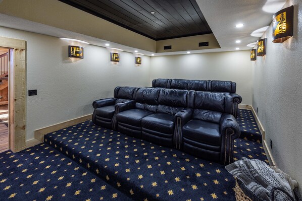 Une salle de cinéma maison avec un canapé en cuir noir, une moquette à motifs d’étoiles et des luminaires fixés au mur.