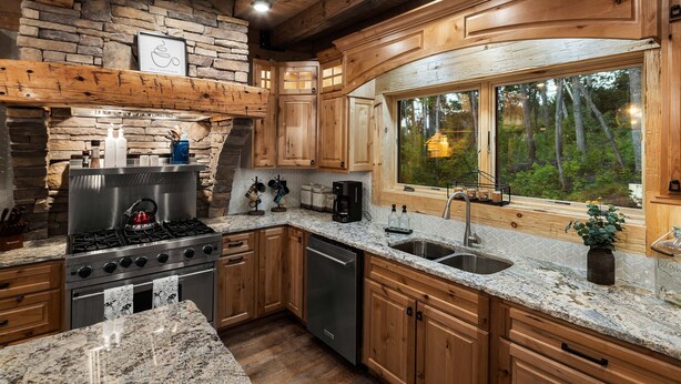 A modern kitchen with granite countertops, wooden cabinets, a built-in stove, and a large window offering a view of the forest. - Smoky Mtn Luxury: Views, Theater, Outdoor Kitchen (Sevierville)