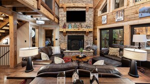 A spacious living room with a stone fireplace, leather sofas, and a wooden ceiling. - Smoky Mtn Luxury: Views, Theater, Outdoor Kitchen (Sevierville)