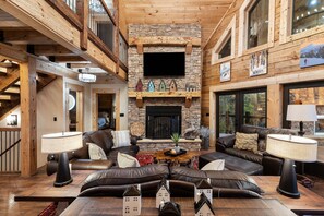 A spacious living room with a stone fireplace, leather sofas, and a wooden ceiling. - Smoky Mtn Luxury: Views, Theater, Outdoor Kitchen (Sevierville)