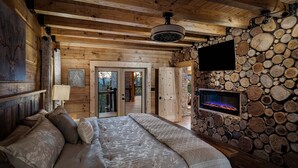 A cozy bedroom with a large bed, a fireplace, and a stone wall. - Smoky Mtn Luxury: Views, Theater, Outdoor Kitchen (Sevierville)