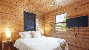 A wooden-paneled bedroom with a bed, bedside lamps, a window, and a mounted television.