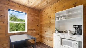 A wooden-paneled room with a window, a white cabinet with kitchen appliances, and a small table.