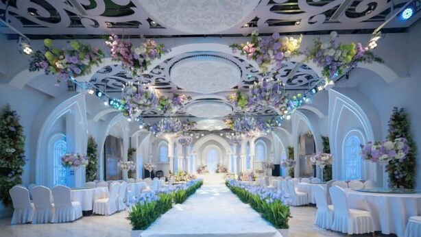 An indoor venue with a central aisle, white chairs, and floral decorations.