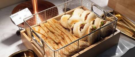 A metal basket containing various food items, including flatbreads and buns, on a table with a copper base.