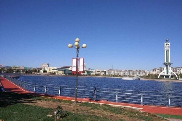 A riverside walkway with a red path, a lamp post, and a tower in the background. - Jinxin Hostel (Laoling)