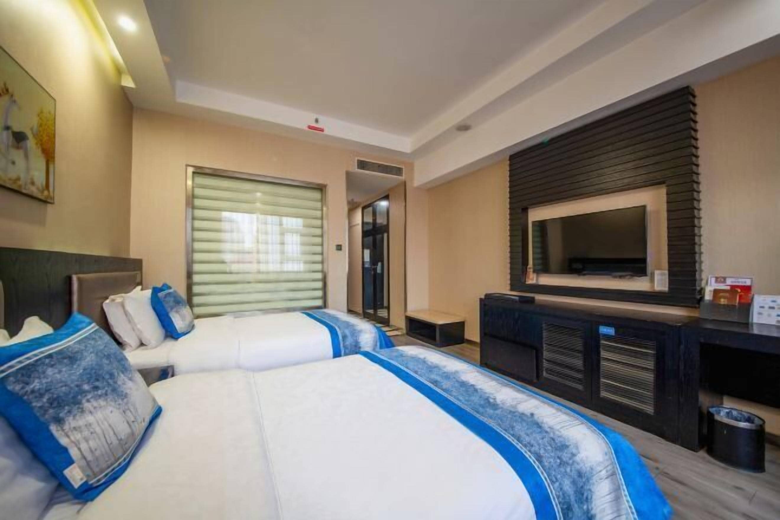 Une chambre d’hôtel avec deux lits, une télévision, un bureau et une fenêtre avec des stores.