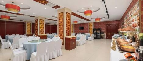 A banquet hall with round tables, white chairs, and a buffet area.