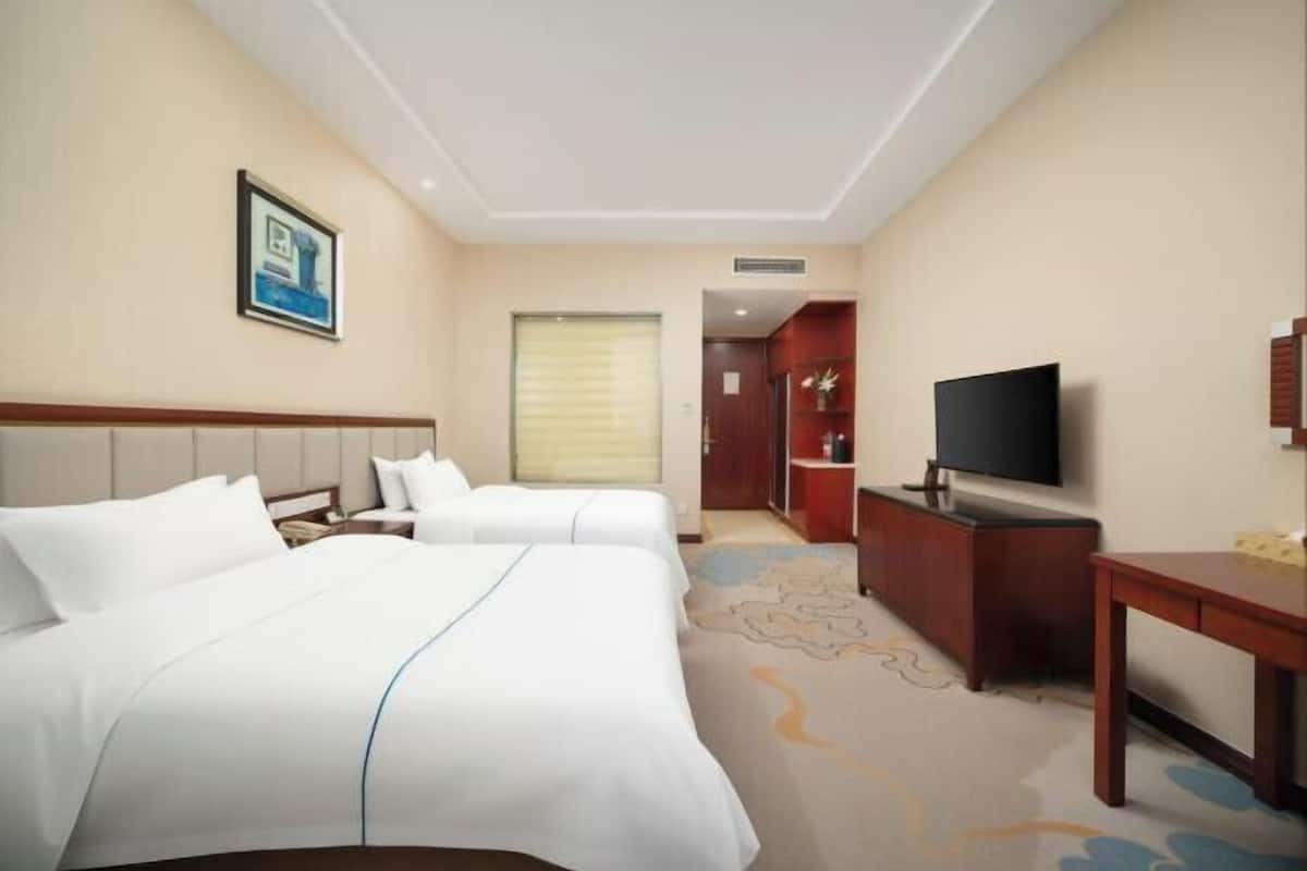 A hotel room with two beds, a television, a desk, and a bathroom visible through an open door.