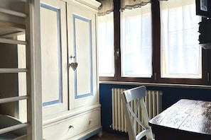 A room with a white wardrobe with blue trim, a radiator, a wooden table, and a chair.