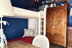 A bunk bed with a ladder, a white chair, a wooden wardrobe, and a bookshelf against a blue wall.